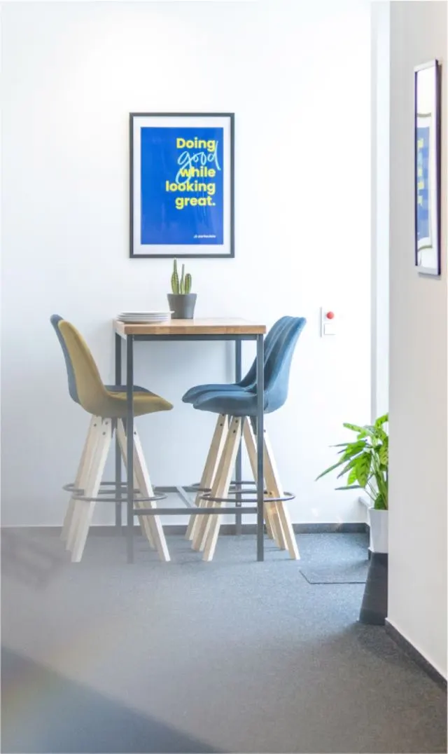 Sitzecke im Particulate-Büro: Stehtisch mit Hockern, darüber ein Poster mit dem Spruch „Doing good while looking great.“
