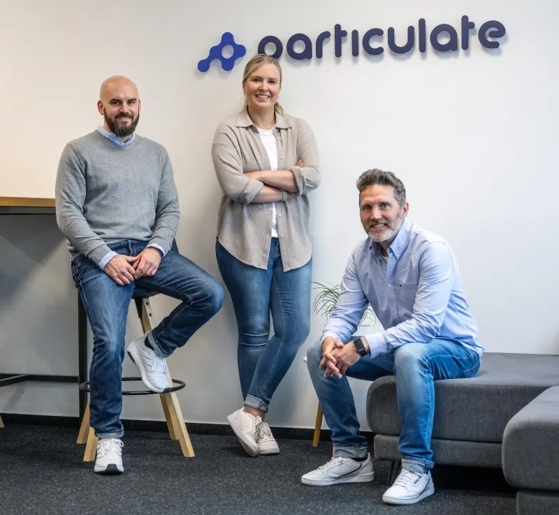 Das Gründerteam von Particulate vor dem Firmenlogo im Büro in Koblenz, von links: Stefan Fink, Stephanie Keßler und Stefan Pandorf